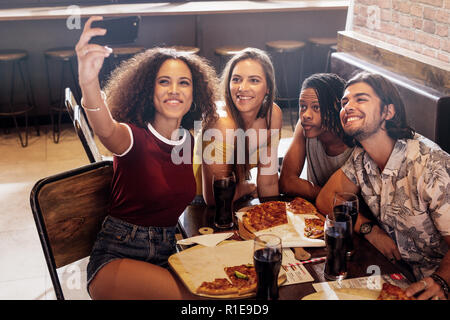 Jeune femme en tenant avec des amis selfies assis à un restaurant. Groupe d'amis à multi-ethnique de la capture d'un café en selfies téléphone intelligent. Banque D'Images