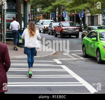 CHARLOTTE, NC, USA-11/8/18 : une femme sur un scooter électrique traverse une rue dans le passage pour piétons, tandis que son compagnon rides à venir. Banque D'Images