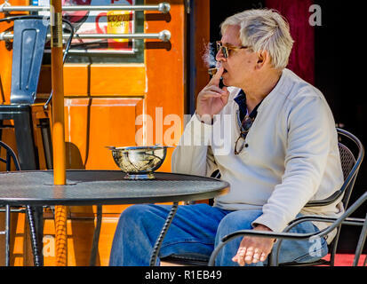 Un homme fume un cigare à une table en face d'Allume Cigare Lounge sur la rue Dauphin, le 3 novembre 2018, à Mobile, Alabama. Le salon, qui a ouvert ses portes au printemps 2 Banque D'Images