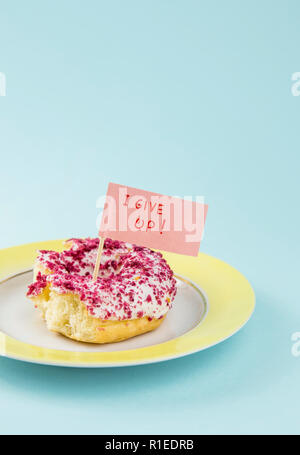 À moitié mangé donut avec glaçage rose et blanc sur plaque jaune avec remise d'un drapeau texte : J'abandonne, sur fond bleu. Studio shot conceptuel de nous Banque D'Images