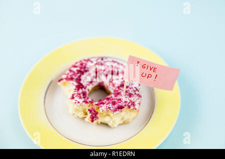 À moitié mangé donut avec glaçage rose et blanc sur plaque jaune avec remise d'un drapeau texte : J'abandonne, sur fond bleu. Studio shot conceptuel de nous Banque D'Images