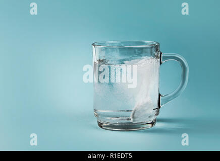 Vue latérale du pain killer soluble dans l'eau bouillonnante de dissolution, ensemble tasse en verre clair, isolé sur fond bleu. Banque D'Images