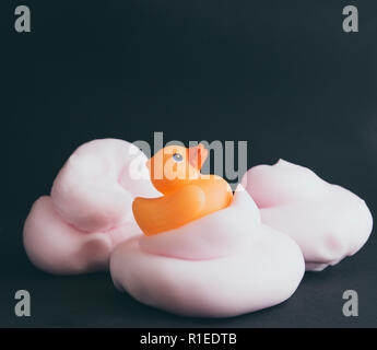 Canard en caoutchouc orange sur le tas de mousse rose isolé sur fond noir. Banque D'Images