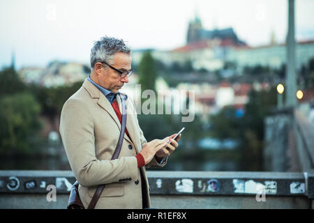 Woman with smartphone debout sur un pont dans la ville, la messagerie texte. Banque D'Images