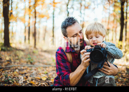 Un père et un petit garçon dans une forêt d'automne, prendre des photos avec un appareil photo. Banque D'Images