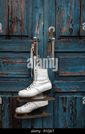 Vintage paire de patins à glace blanc accroché sur la porte rustique aux tons bleu, Banque D'Images
