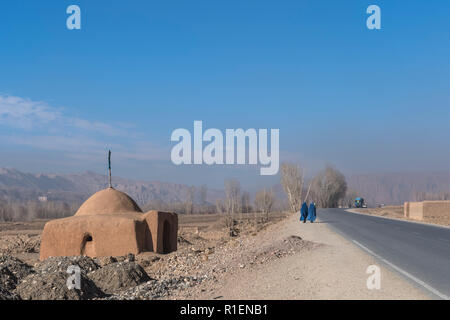 2 Femmes portant Burqa bleu marche sur route entrant dans la vallée de Bamyan avec un lieu de culte et les montagnes en arrière-plan, la province de Bamyan, Afghanistan Banque D'Images