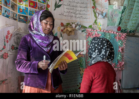 Girl est enseigné en anglais par Enseignante en Co-Educational School Situé à Hillside village troglodyte, province de Bamyan, Afghanistan Banque D'Images