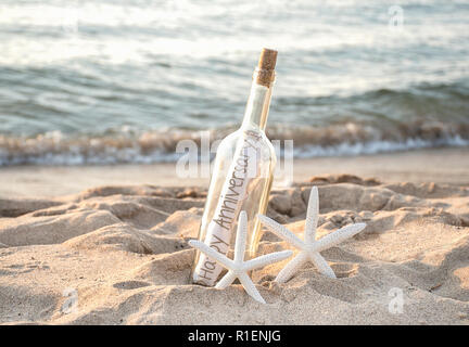 Paire d'étoiles blanches dans le sable de la plage avec happy anniversaire message dans une bouteille à la mer Banque D'Images