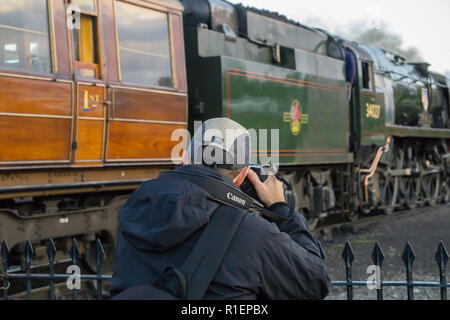 Close up mâle isolé photographe, vue arrière, prendre des photos de vintage UK train à vapeur et voitures en attente de départ, gare ferroviaire patrimoniale. Banque D'Images