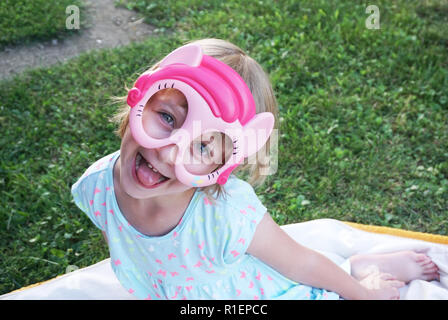 Heureux adorable petite fille faire drôle de visage avec masque sur elle et à la recherche dans l'appareil photo Banque D'Images