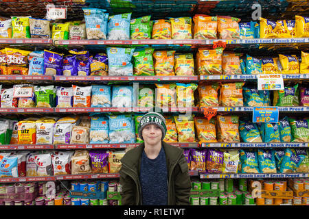 Neuf ans garçon en face d'étagères de magasin de chips de pommes de terre, les crics, Midtown, New York, États-Unis d'Amérique. Banque D'Images