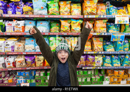 Neuf ans garçon en face d'étagères de magasin de chips de pommes de terre, les crics, Midtown, New York, États-Unis d'Amérique. Banque D'Images