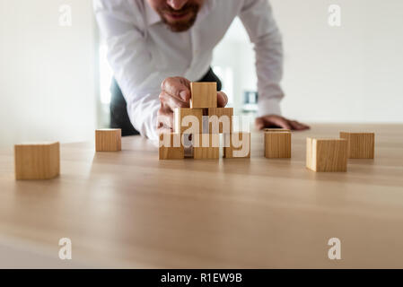 Businessman leaning à monter avec pyramide avec blocs de bois vierge sur office 24. Démarrage d'une entreprise de conception et de vision. Banque D'Images