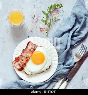 Assiette de petit-déjeuner avec des œufs, du bacon et des toasts de pain de seigle sur un fond gris. Petit-déjeuner anglais, jus d'Orange Banque D'Images