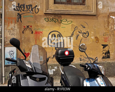 Vespa scooters style noir en stationnement sur rue à Florence, Toscane Italie en face de centre ville immeuble avec mur couvert de graffitis Banque D'Images