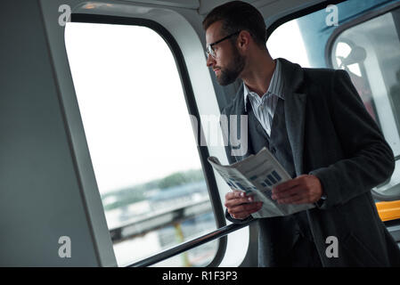 Voyage d'affaires. Young businessman standing dans la holding newspaper en regardant par la fenêtre d'affichage de la fenêtre d Banque D'Images