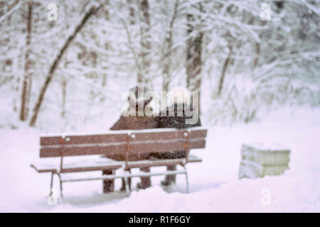 Couple de personnes âgées assis sur un banc en bois dans un jour de neige de l'hiver, à pied et la vie ensemble, arrière-plan flou Banque D'Images