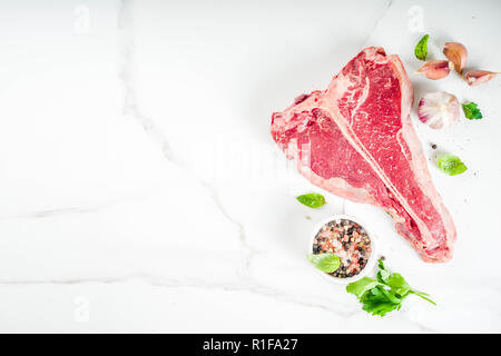 Matières de la viande fraîche, t-bone steak de boeuf aux épices et herbes sur une planche à découper, béton table top view copy space Banque D'Images