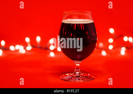 Verre verre de bière noire ou porter la bière avec les lumières de Noël sur fond rouge Banque D'Images