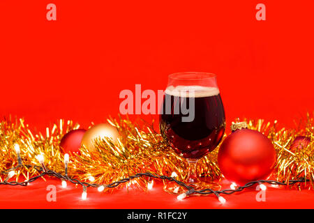 Verre verre de bière porter ou bière noire avec des lumières de Noël et de guirlandes de Noël sur fond rouge Banque D'Images