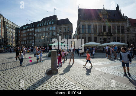 Marktplatz, Brême. Deutschland Allemagne. Une scène à l'ensemble de la place du marché où les enfants participeront à un homme créant de grandes bulles qui flottent dans l'air. C'est une journée ensoleillée et le soleil est à l'origine de longues ombres d'être exprimés par les personnes dans la scène. Banque D'Images