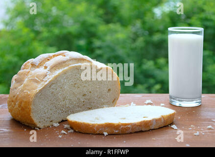 Miche de pain blanc, couper un morceau de pain et du lait dans un verre. Sur un fond de bois. Banque D'Images