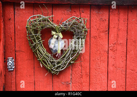 Fait à la main traditionnel twig coeur accroché sur porte en bois rouge avec marteau. Banque D'Images