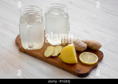 Pot en verre de thé au gingembre avec des ingrédients sur planche de bois blanc sur fond de bois, vue de côté. Libre. Banque D'Images