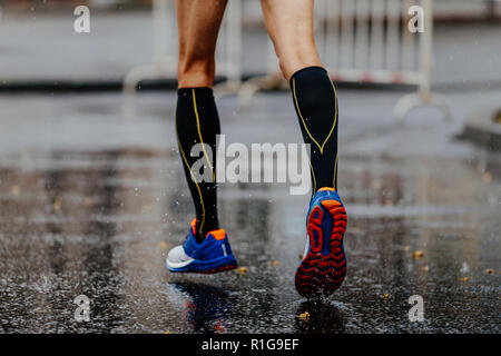 Pieds dans des chaussettes de compression runner mâle d'exécution sur l'asphalte humide Banque D'Images