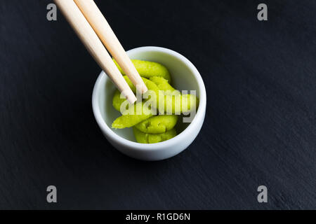 Wasabi raifort japonais dans de petites baguettes avec bol blanc sur noir plaque ardoise cuisine. La cuisine asiatique typique d'épices. Banque D'Images