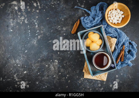 Émaillé bleu tasse de thé, des bâtons de cannelle, d'anis étoile et des sablés sur un fond sombre. Vue d'en haut. L'espace pour le texte. Banque D'Images
