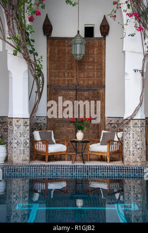 18-04-11. Marrakech, Maroc. Riad typiquement marocain courtyars avec de grandes portes sculptées, une piscine de refroidissement, d'une piscine, de chaises et de roses dans un vase. Photo Banque D'Images