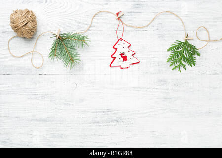Guirlande de noël faites de branches d'arbres conifères et arbres de Noël rouge contre l'arrière-plan en bois blanc avec copie espace. Banque D'Images