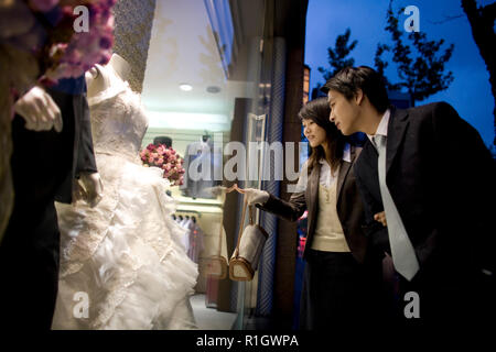 Young adult couple looking at a wedding dress à travers une vitrine au crépuscule. Banque D'Images