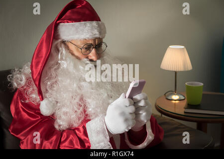 Profil de Père Noël (ou Saint Nicolas) assis dans la table à la maison à l'écran du smartphone. Banque D'Images