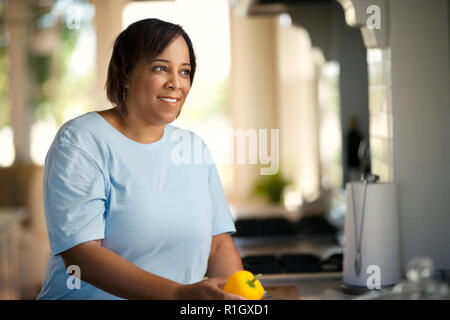 Femme tenant un poivron jaune et à la recherche d'attention à une cuisine lumineuse et aérée. Banque D'Images