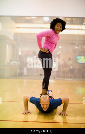 Portrait d'une jeune femme debout sur le dos d'une mid-adult man doing une presse dans une salle de sport. Banque D'Images