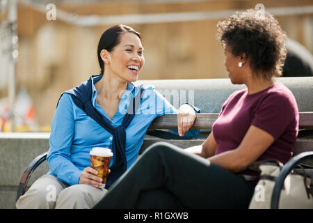 Two smiling women having a conversation, alors qu'il était assis dans un parc de la ville. Banque D'Images