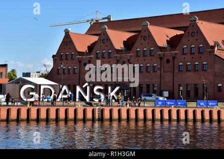 Vue urbaine avec les touristes, inscription 'Gdansk' en blanc et rouge et l'Orchestre Philharmonique Baltique polonaise sur l'île Ołowianka, fleuve Motlawa, Gdansk, Pologne Banque D'Images