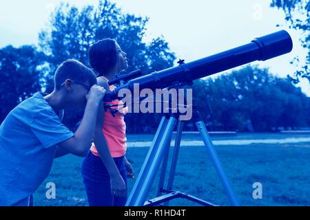 L'adolescence avec un télescope dans la soirée. Les enfants à la recherche avec intérêt dans le ciel. Banque D'Images