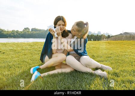 Confort adolescente pleurant, contrariée, triste ami. Les filles sont assis sur l'herbe verte dans le parc. Banque D'Images