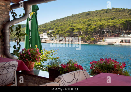 Restaurant méditerranéen près de la mer bleue. Pots à fleurs roses, debout près de la table et une descente en métal. Collines couvertes de vert verdan Banque D'Images