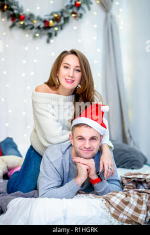 Famille heureuse, père et mère dans la matinée dans la chambre décorée pour Noël. Père à Santa's hat portant sur le lit et la mère assis sur lui. La nouvelle année et thème de Noël. Ambiance de vacances Banque D'Images