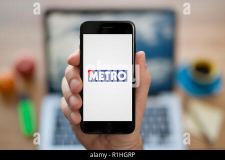 Un homme se penche sur son iPhone qui affiche le logo du métro, tout en s'assit à son bureau informatique (usage éditorial uniquement). Banque D'Images