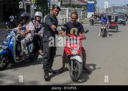 L'agent de police de la charia islamique (Wilayatul Hisbah) vu l'arrêt d'un automobiliste vêtu d'un court-circuit au cours de la routine des raids à Lhokseumawe. Les agents de la Police de la charia islamique (Wilayatul Hisbah) fournir des sarongs pour ceux qui violent la loi de la charia islamique par la force dans la ville de Lhokseumawe, Aceh est la seule province de l'Indonésie qui a la plus grande population de musulmans dans le monde, qui met en œuvre la charia islamique comme la commission de la bastonnade et mener des raids de routine pour ceux qui sont bien habillés pour femmes et des shorts pour hommes. Banque D'Images