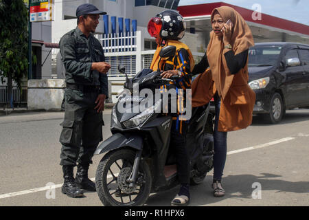 L'agent de police de la charia islamique (Wilayatul Hisbah) vu l'arrêt d'un automobiliste de porter des vêtements serrés au cours de la routine à Lhokseumawe raids. Les agents de la Police de la charia islamique (Wilayatul Hisbah) fournir des sarongs pour ceux qui violent la loi de la charia islamique par la force dans la ville de Lhokseumawe, Aceh est la seule province de l'Indonésie qui a la plus grande population de musulmans dans le monde, qui met en œuvre la charia islamique comme la commission de la bastonnade et mener des raids de routine pour ceux qui sont bien habillés pour femmes et des shorts pour hommes. Banque D'Images