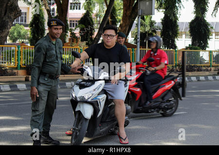 L'agent de police de la charia islamique (Wilayatul Hisbah) vu l'arrêt d'un automobiliste vêtu d'un court-circuit au cours de la routine des raids à Lhokseumawe. Les agents de la Police de la charia islamique (Wilayatul Hisbah) fournir des sarongs pour ceux qui violent la loi de la charia islamique par la force dans la ville de Lhokseumawe, Aceh est la seule province de l'Indonésie qui a la plus grande population de musulmans dans le monde, qui met en œuvre la charia islamique comme la commission de la bastonnade et mener des raids de routine pour ceux qui sont bien habillés pour femmes et des shorts pour hommes. Banque D'Images