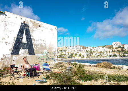 Plage à Santa Pola Espagne, un pêcheur senior relaxant sur la jetée en novembre, mural grande lettre Un énorme adulte senior Banque D'Images