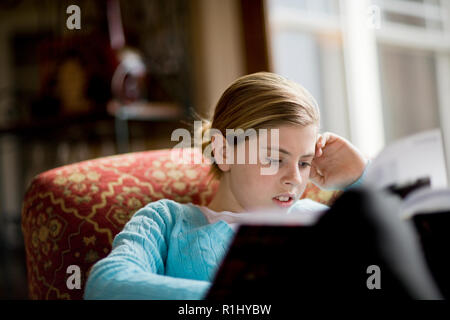 Girl sitting in armchair reading Banque D'Images